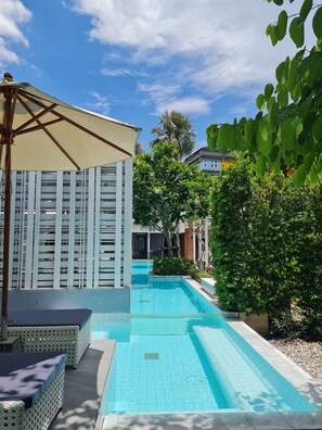 A swimming pool with a pergola and lounge chairs, surrounded by greenery and a building with a white facade. - Treevana Club Chiangmai (Chiang Mai)