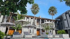 Área da piscina com espreguiçadeiras e guarda-sóis, uma piscina e um edifício com varandas.