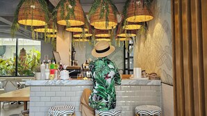 Interior de restaurante com área de bar, luminárias de vime penduradas e piso estampado.