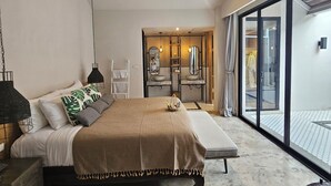 Quarto com cama, mesas de cabeceira, luminária pendente, ar condicionado e vista para o exterior por uma porta de vidro deslizante.