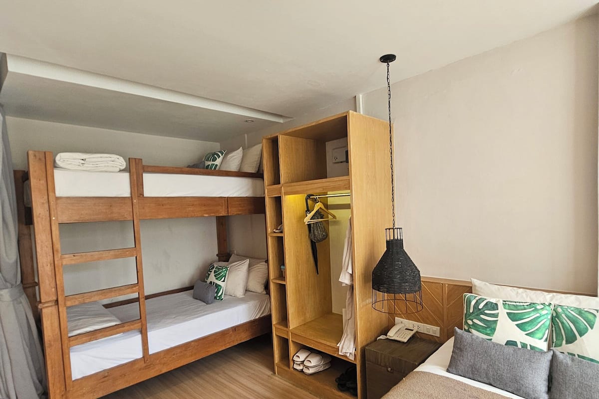 Una habitación con literas, un armario de madera, una mesita de noche, una lámpara colgante y una cama con almohadas.