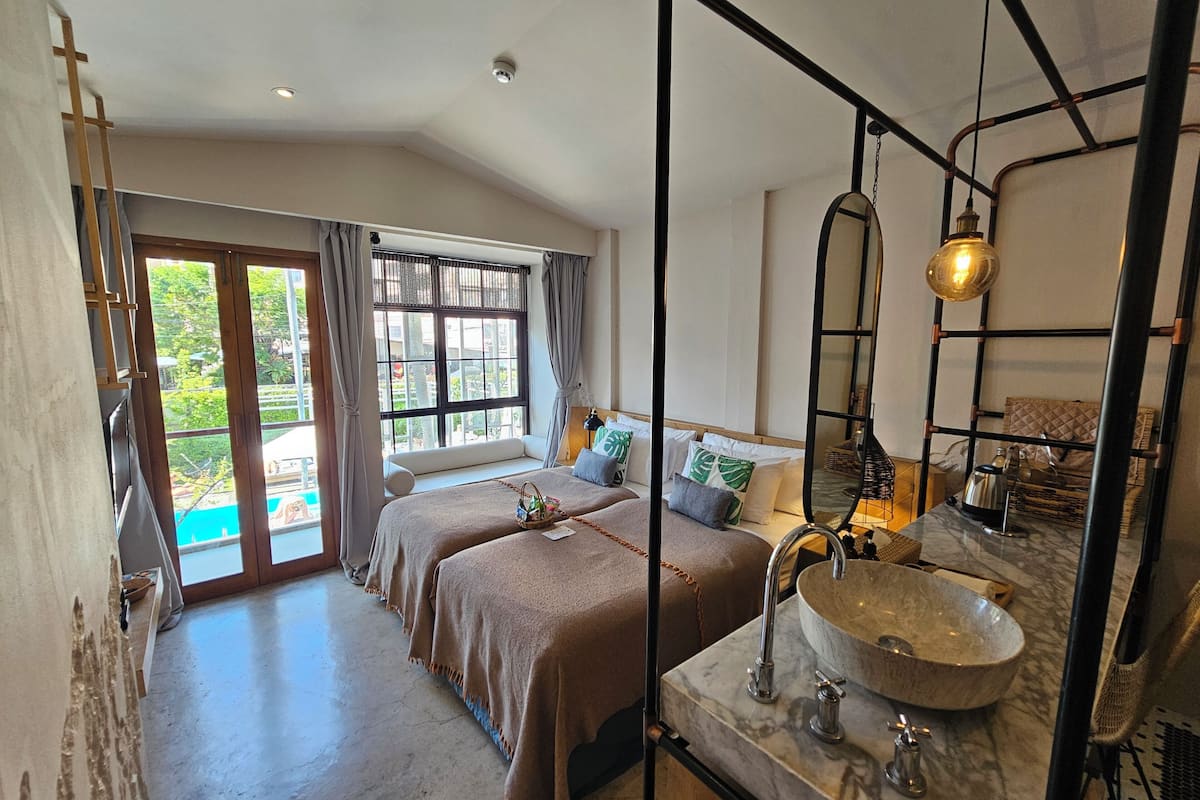 Habitación de hotel con dos camas, un ventanal grande, un baño con lavamanos de mármol y vistas al exterior.