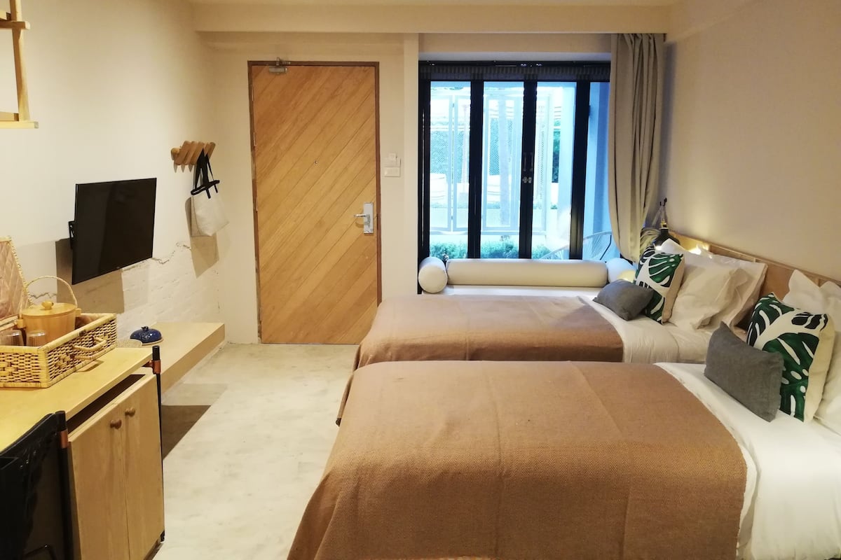 Habitación de hotel con dos camas, una puerta de madera, televisión, escritorio y ventana con vistas.