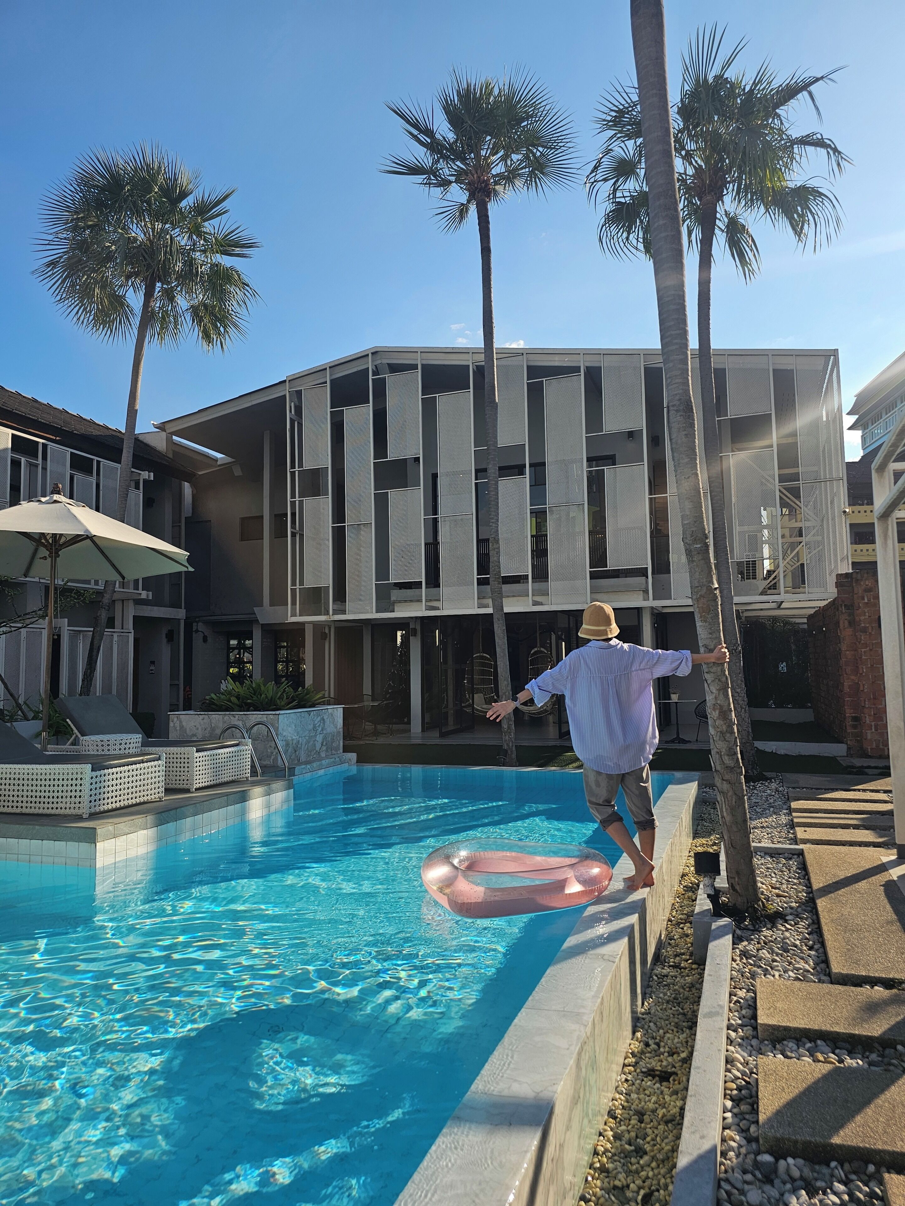 A swimming pool with lounge chairs, palm trees, and a modern building with large windows.