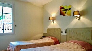 A hotel room with two beds, a window with a view, and wall-mounted lamps. - Hotel de la Montagne Noire (Dourgne)