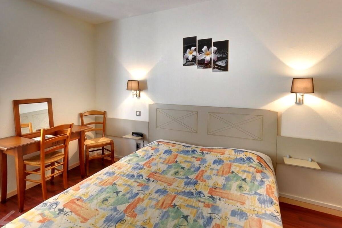 Ein Schlafzimmer mit einem Bett, einem Schreibtisch, zwei Stühlen, einem Fenster und Wandlampen.
