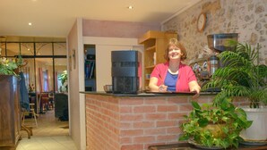 A reception area with a brick counter, a coffee machine, and a clock on the wall. - Hotel de la Montagne Noire (Dourgne)