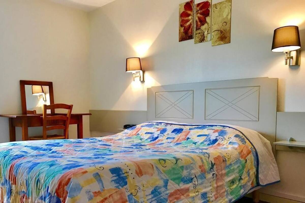 Ein Hotelzimmer mit einem Bett, einem Schreibtisch, zwei Wandleuchten und Kunstwerken an der Wand.