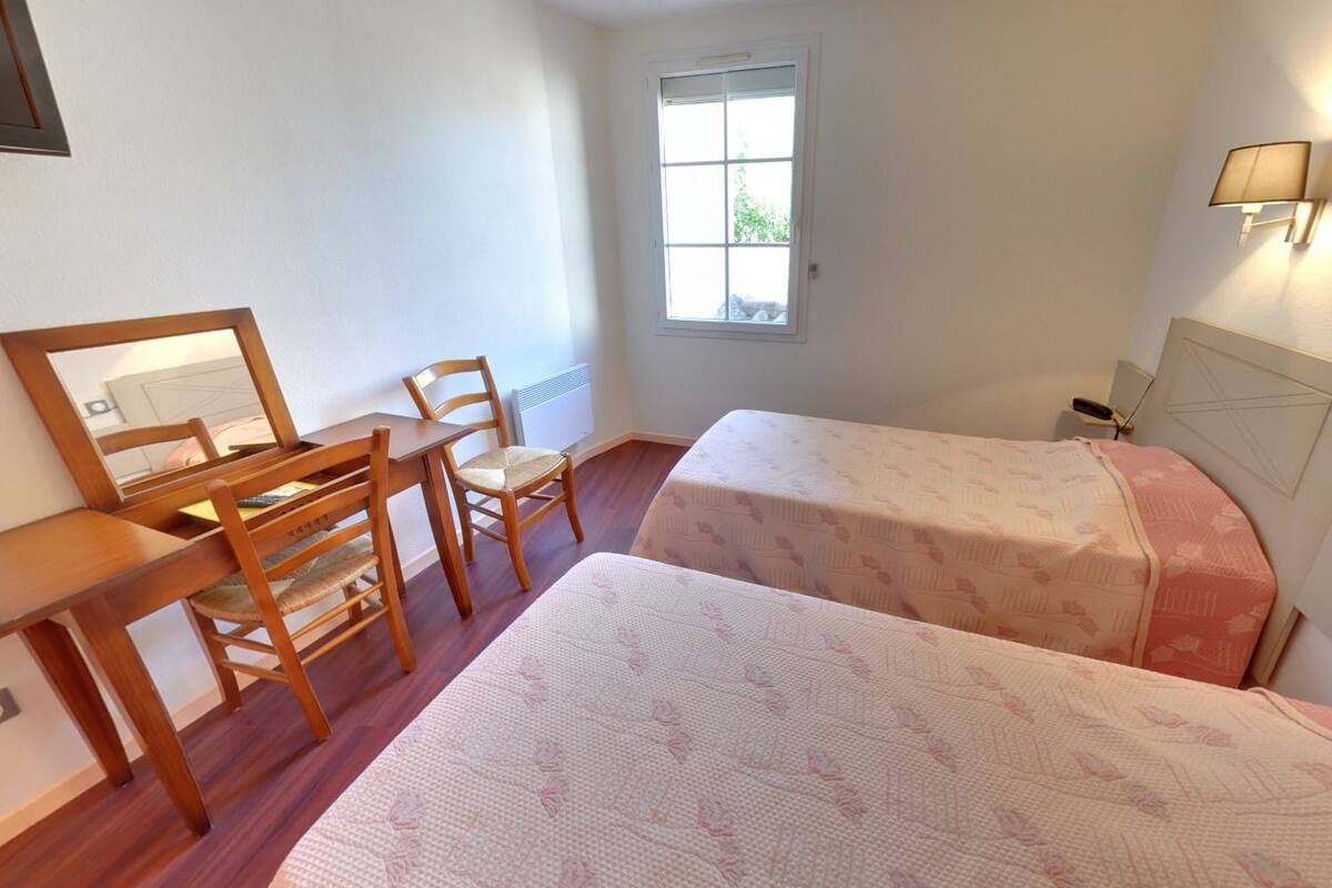 Ein Schlafzimmer mit zwei Betten, einem Schreibtisch, einem Stuhl, einem Fenster und einer Wandlampe.