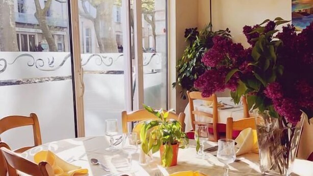 A dining area with round tables, chairs, and a potted plant. - Hotel de la Montagne Noire (Dourgne)