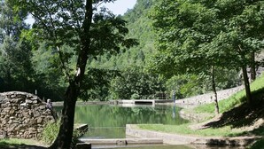 A serene outdoor setting with a stone structure near a calm water body, surrounded by lush greenery and a stone wall. - Hotel de la Montagne Noire (Dourgne)