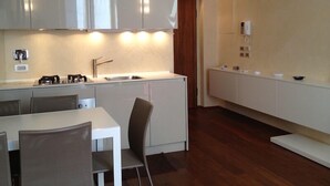 Een moderne keuken met witte kasten, een gasfornuis en een spoelbak. Er is een eethoek met een witte tafel en stoelen.