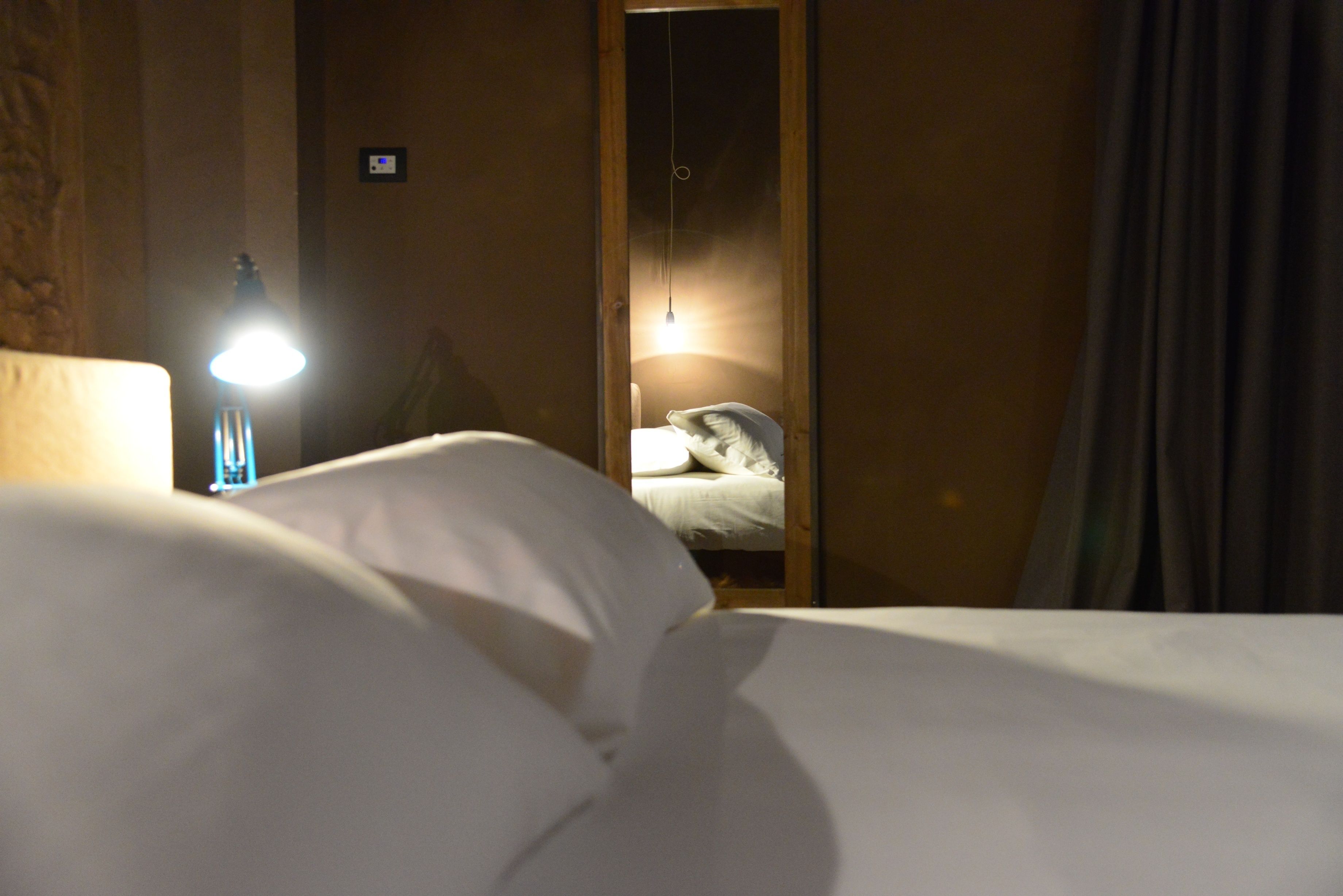 Ein Hotelzimmer mit Bett, Nachttisch mit Lampe und Spiegel, der ein Bett mit Kissen reflektiert.