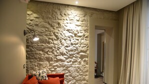 Een woonkamer met een stenen muur, een bank met gestreepte kussens en een brandende wandlamp.