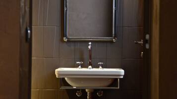 A restroom with a sink, mirror, and a trash can.