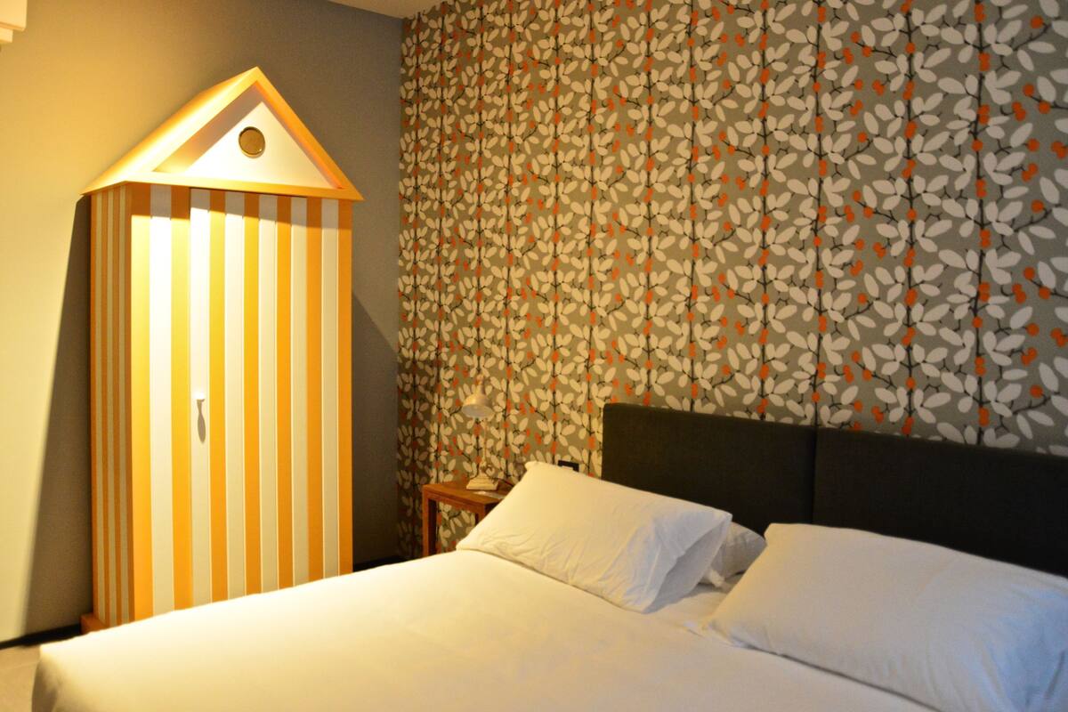 Una habitación de hotel con una cama, una lámpara a rayas y un papel tapiz estampado.