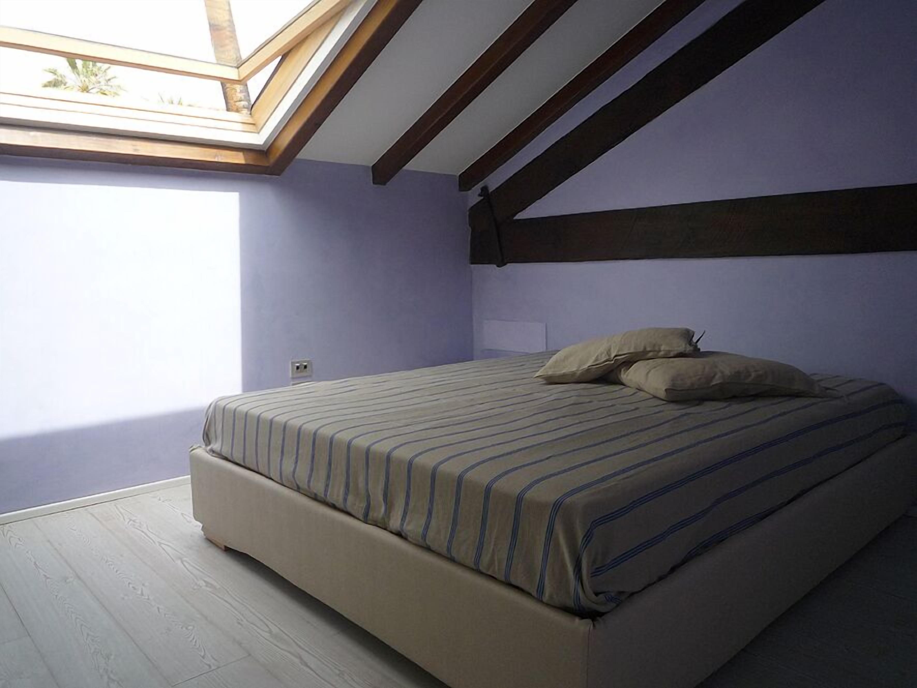 Ein Schlafzimmer mit Oberlicht, einem Bett mit gestreifter Bettwäsche und einem Holzboden.
