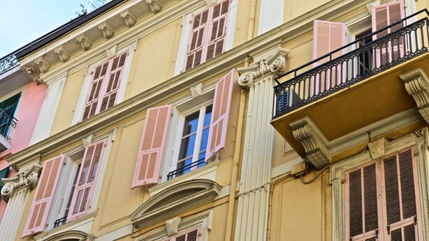 Een meerlaags gebouw met roze en gele gevels, versierde balkons en traditionele luiken.