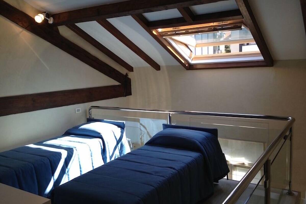 Una habitación con dos camas, vigas de madera, un tragaluz y vistas a edificios.