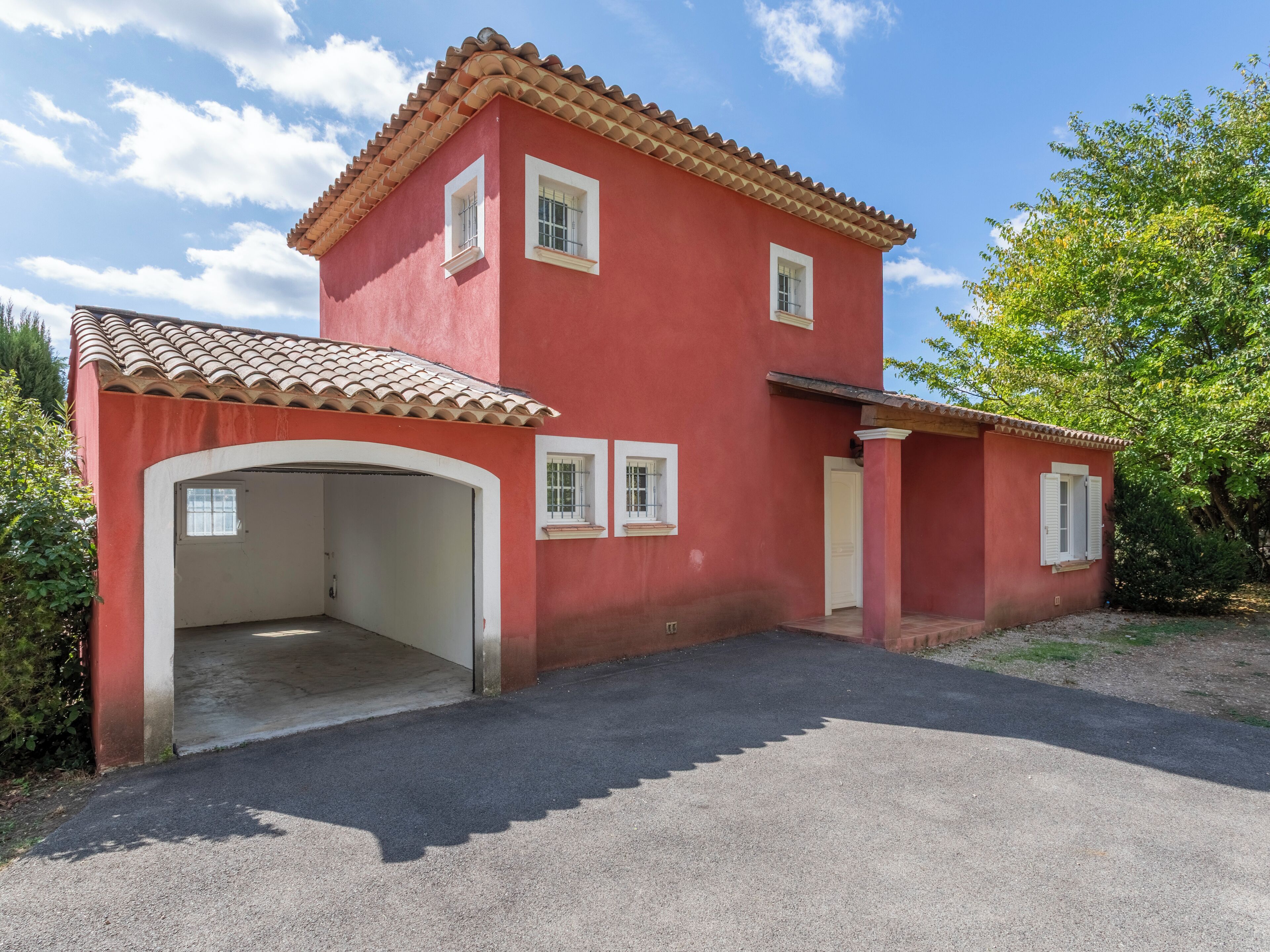 Una casa roja con techo de tejas, garaje y un pequeño porche.