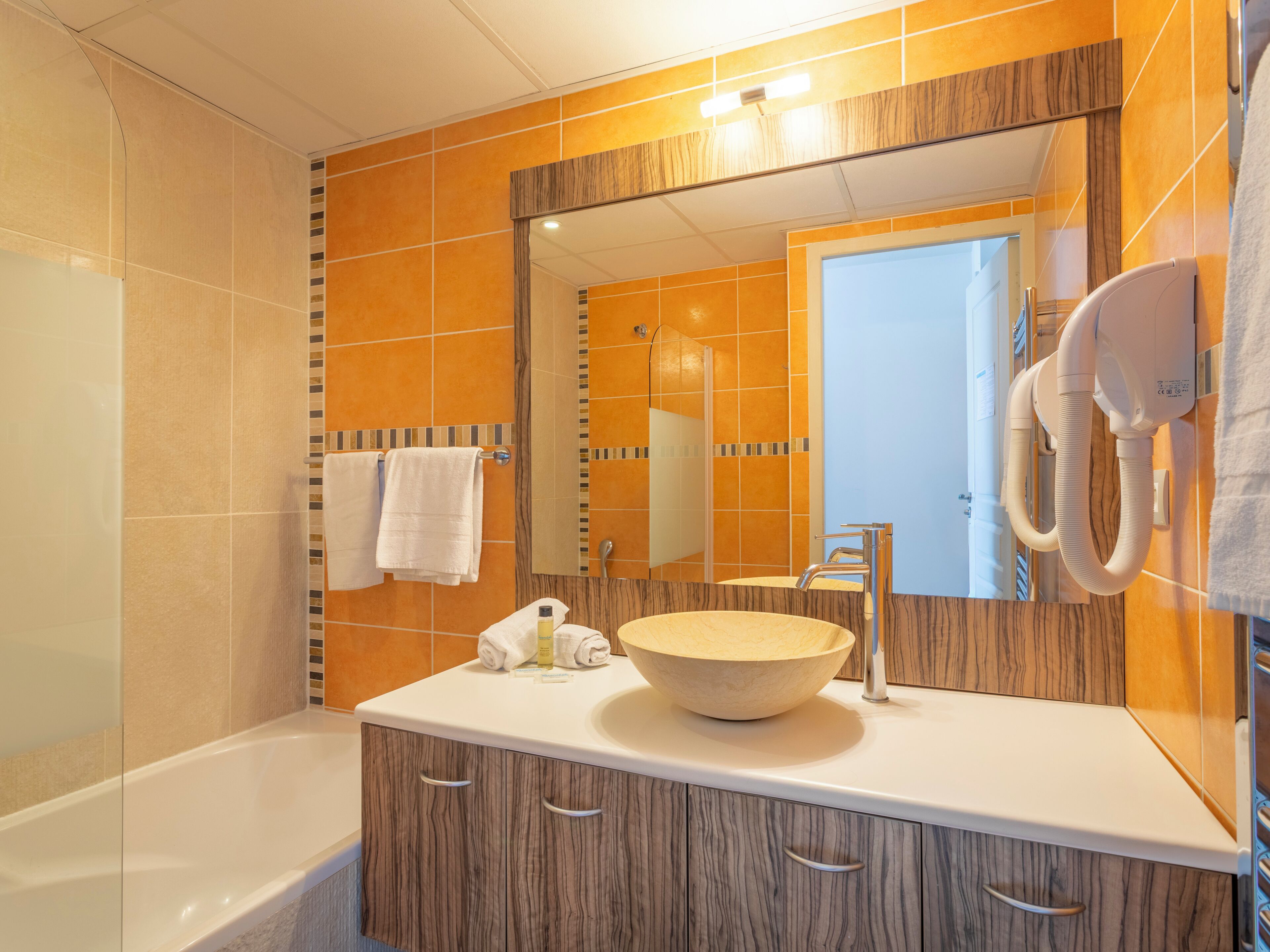A bathroom with a wooden vanity, a large mirror, a white sink, and a towel rack.