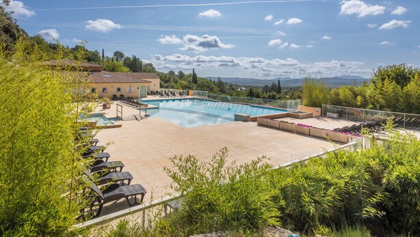 Una piscina con sillas de descanso, un edificio con techo de tejas y un paisaje montañoso al fondo.