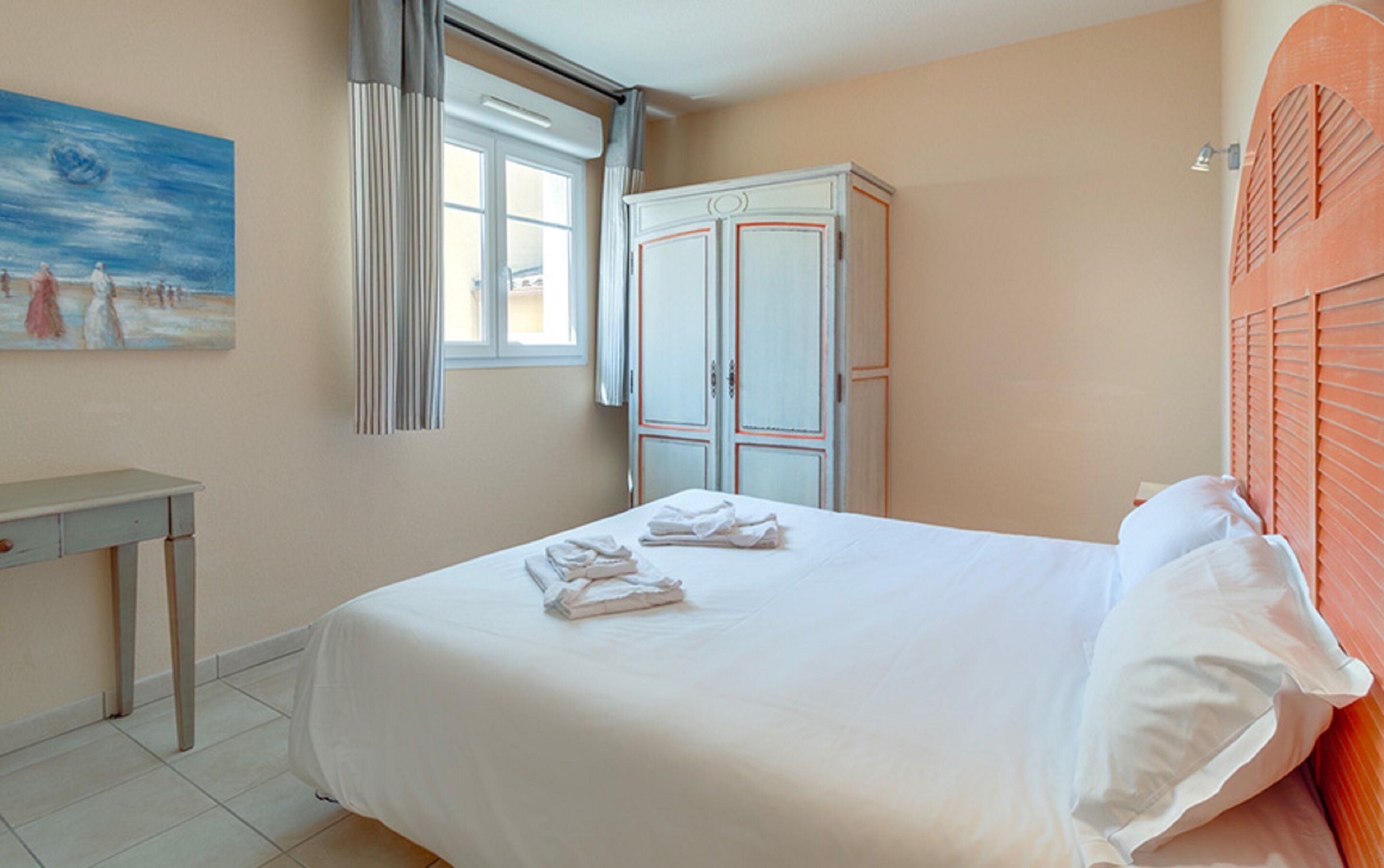 A bedroom with a bed, a wardrobe, a painting, and a window.
