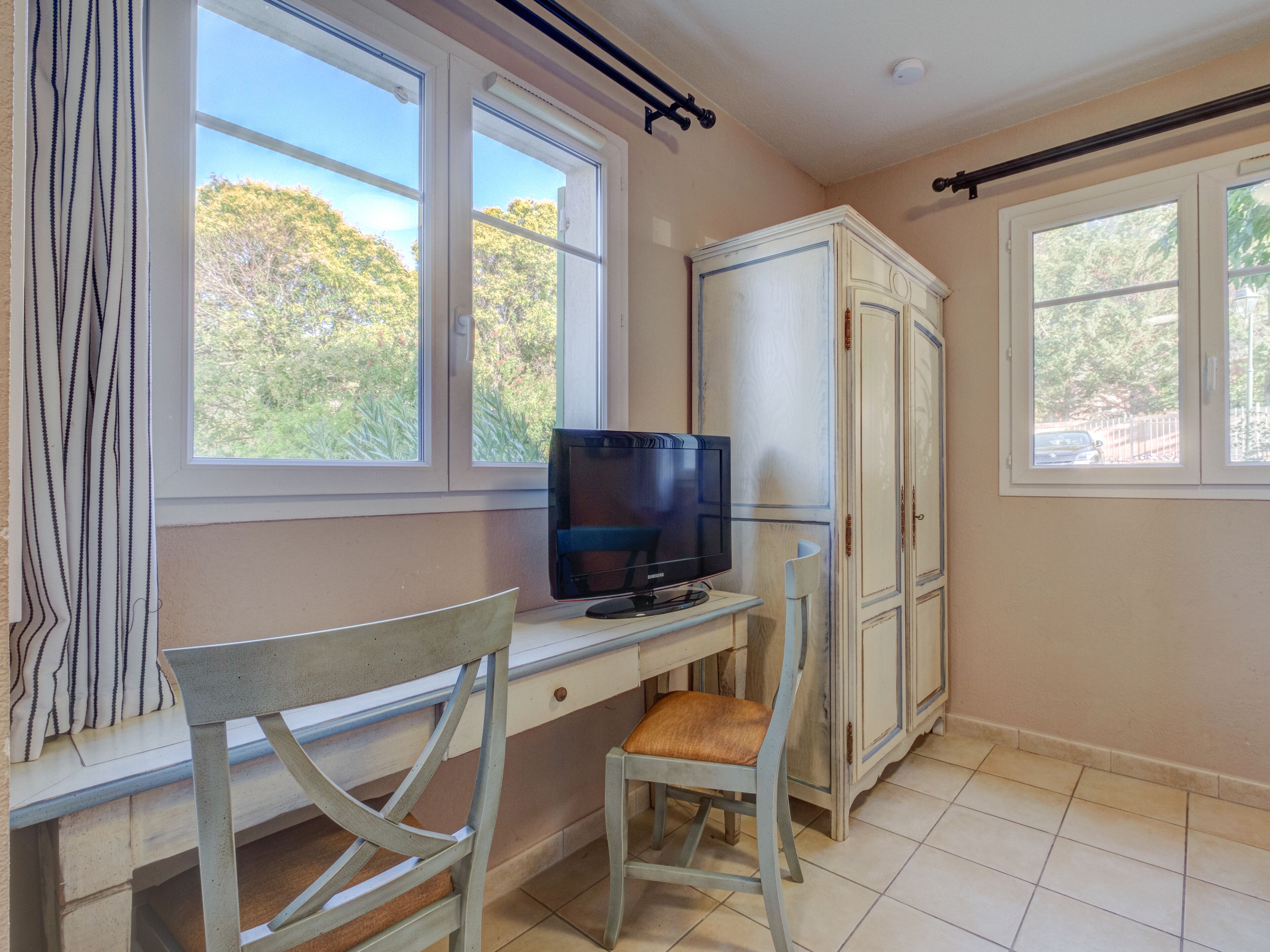 A room with a desk, chair, television, and wardrobe.
