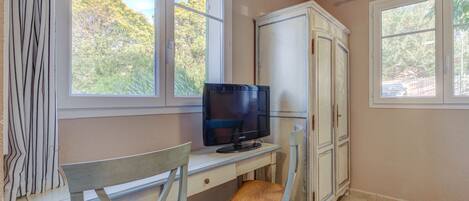 A room with a desk, chair, television, and wardrobe.