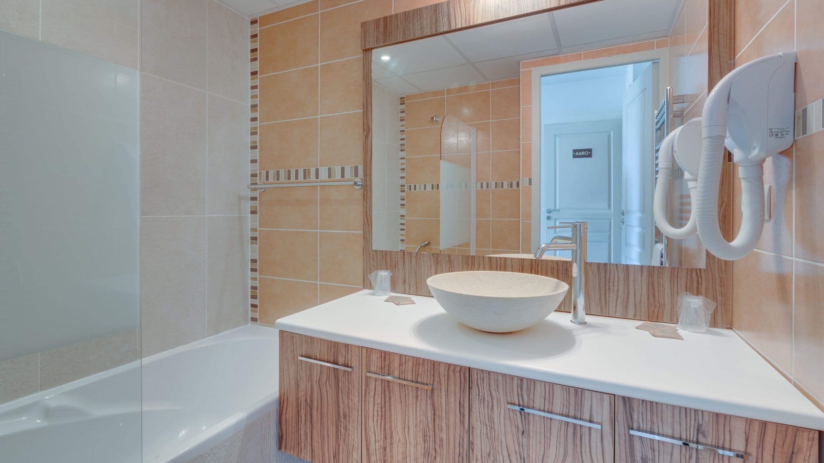 A modern bathroom with a large bathtub, a wooden vanity with a white sink, and a mirror above the vanity.