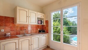 Una cocina con un lavamanos, armarios y una ventana con vistas a un jardín.