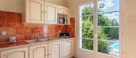 Una cocina con un lavamanos, armarios y una ventana con vistas a un jardín.