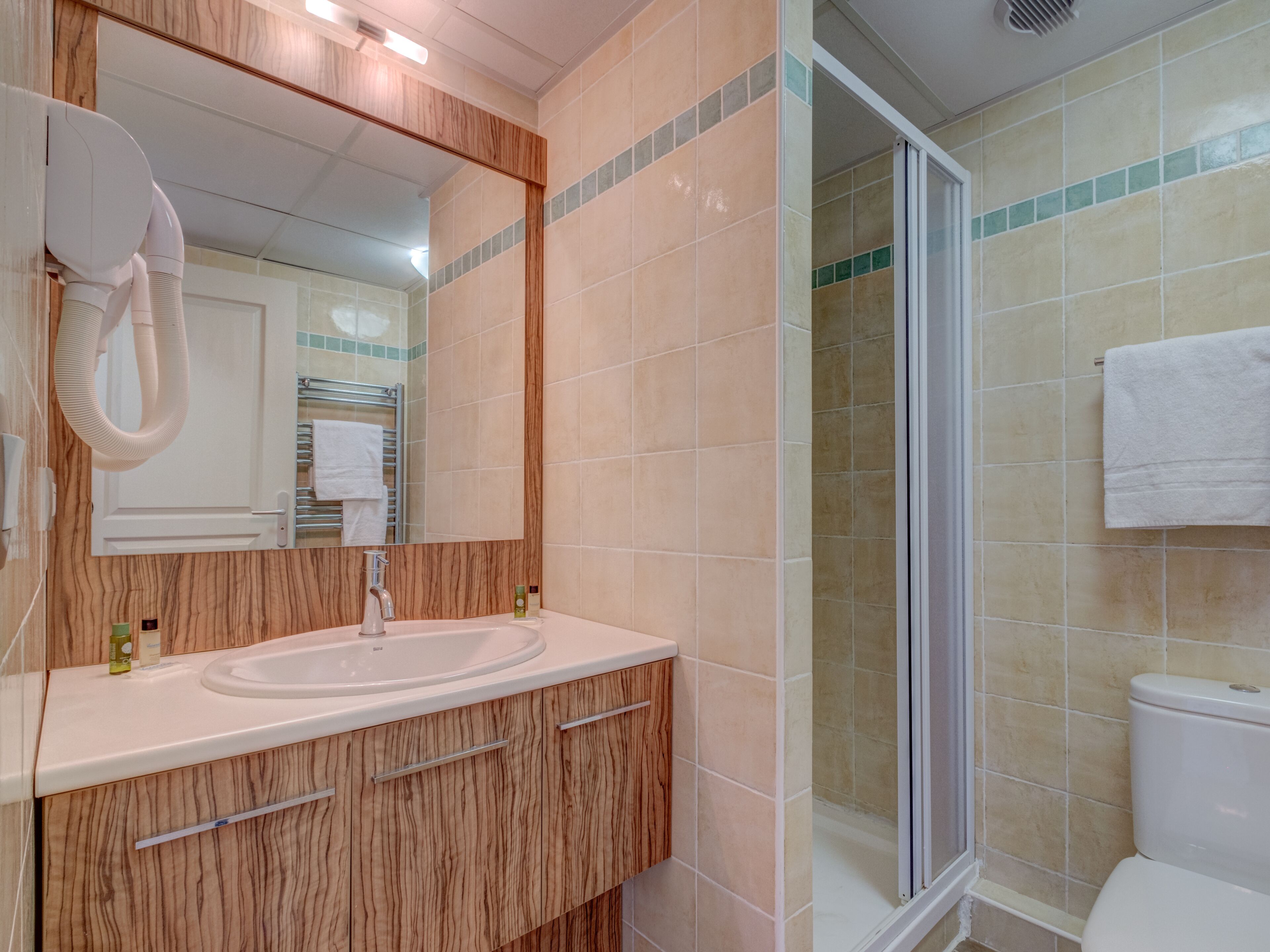 A bathroom with a wooden vanity, a sink, a mirror, a towel rack, and a shower area.