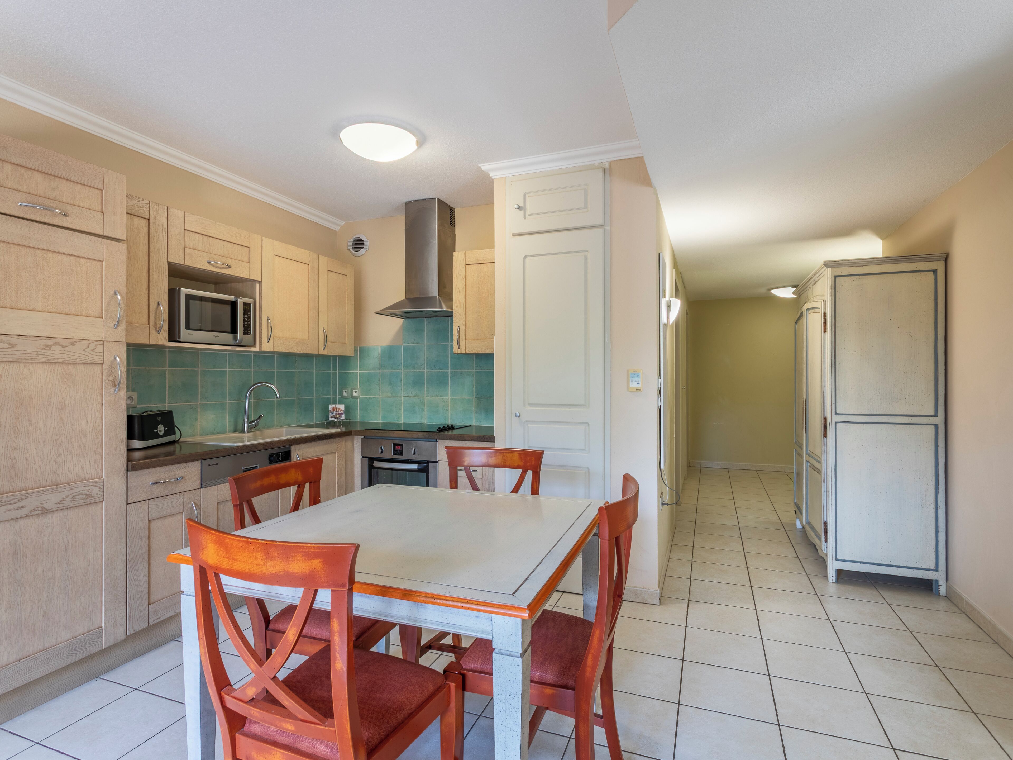 A compact kitchen with wooden cabinets, a microwave, a stove, and a dining table with chairs.
