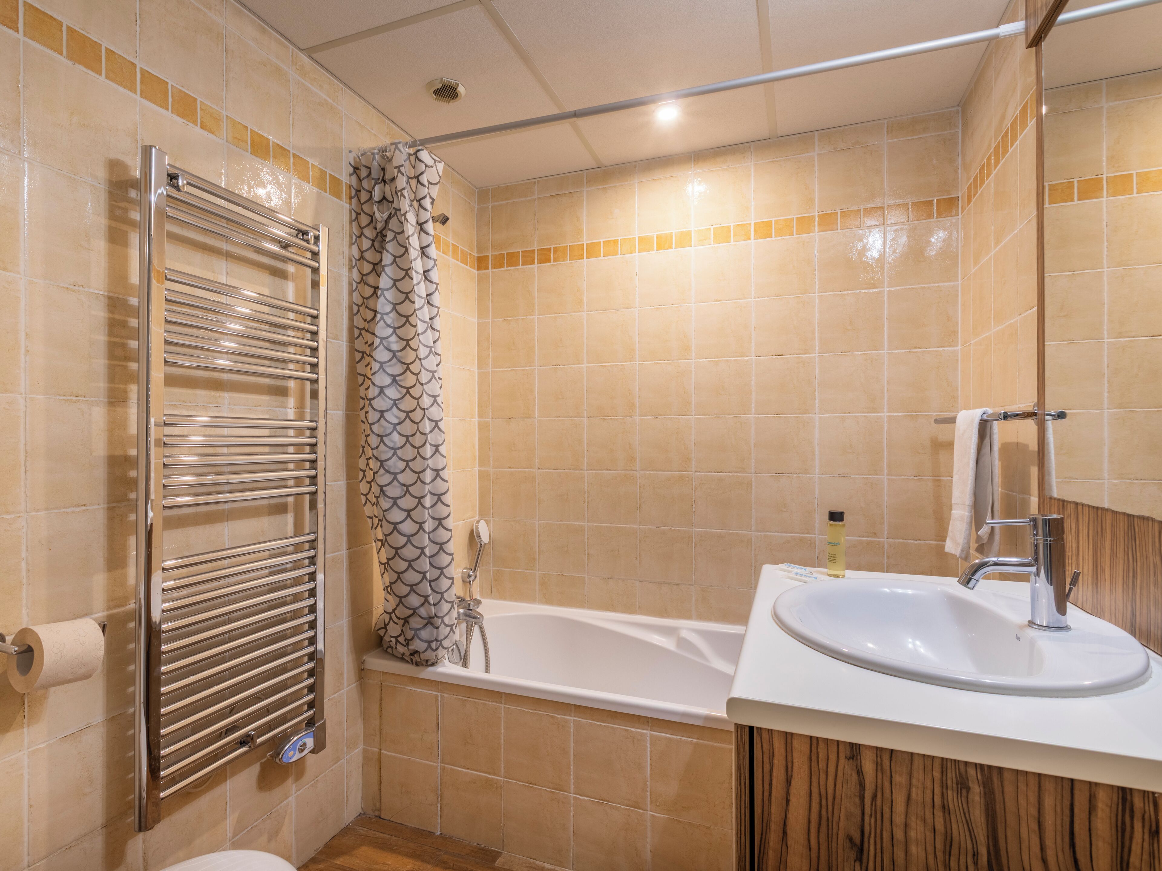 A bathroom with a bathtub, a shower with a patterned curtain, a towel rack, and a sink with a mirror.