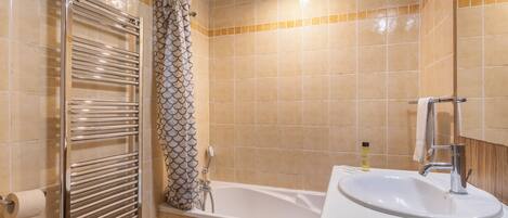 A bathroom with a bathtub, a shower with a patterned curtain, a towel rack, and a sink with a mirror.