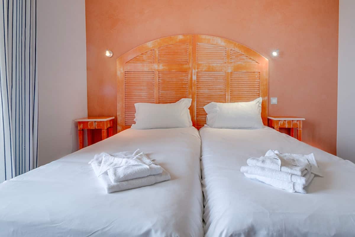Habitación doble con dos camas, cada una con ropa de cama y toallas blancas, un cabecero de madera y dos mesitas de noche.