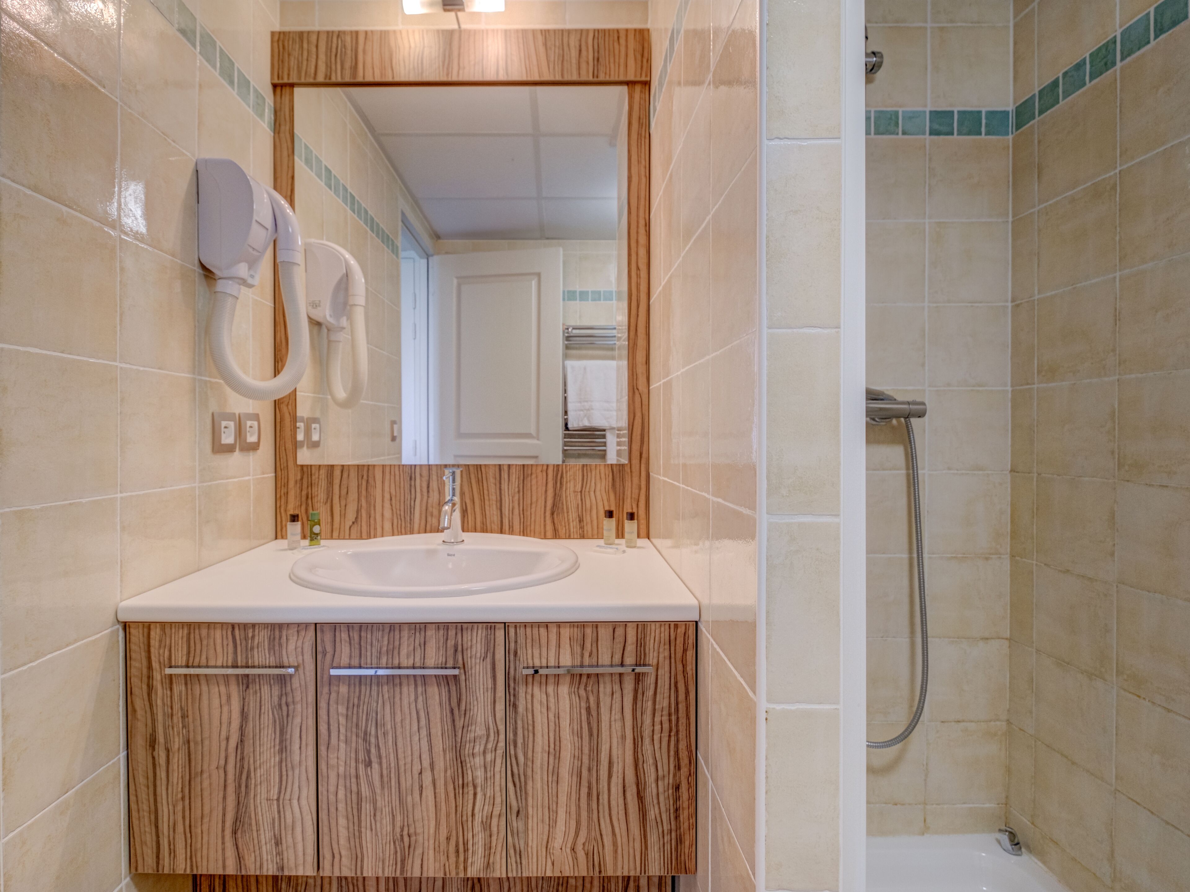 A bathroom with a sink, mirror, wooden cabinets, and a shower.