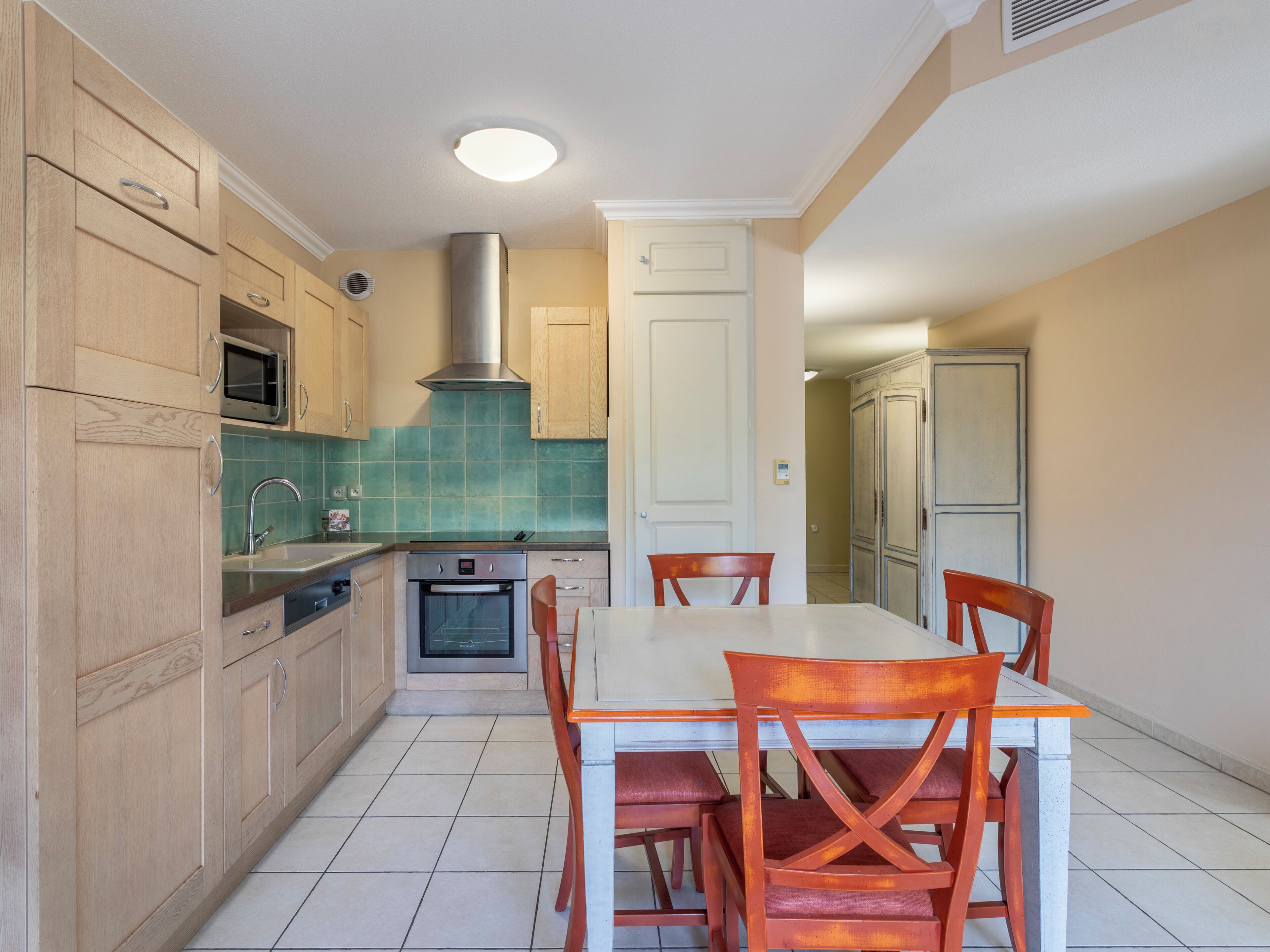 Een keuken met houten kastjes, een magnetron, een fornuis en een eettafel met stoelen.