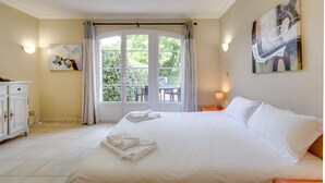 Habitación de hotel con una cama grande, zona de comedor con sillas y una mesa, y vistas a zonas verdes.