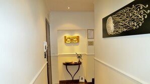 A narrow hallway with wooden flooring, a small table with a globe and a bowl, and a wall-mounted artwork. - Affittacamere La Stazione (La Spezia)