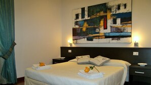 A neatly made bed with pillows and a folded towel, a bedside table with a bowl, and a painting on the wall. - Affittacamere La Stazione (La Spezia)