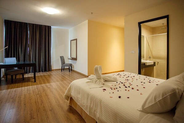 A hotel room with a bed, a desk, a chair, a mirror, and a bathroom visible through an open door.