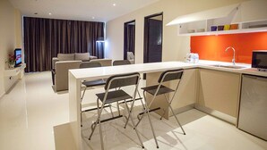 A modern kitchen with a white countertop, two foldable chairs, a dining table, and a built-in sink. - Cathayana Hotel (Kuantan)