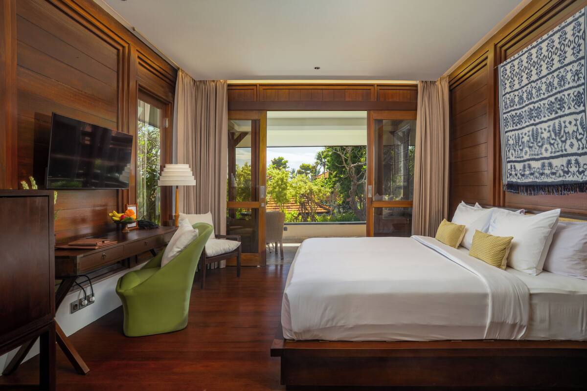 Quarto de hotel com uma cama grande, uma escrivaninha com televisão, uma cadeira verde e uma varanda com vista.