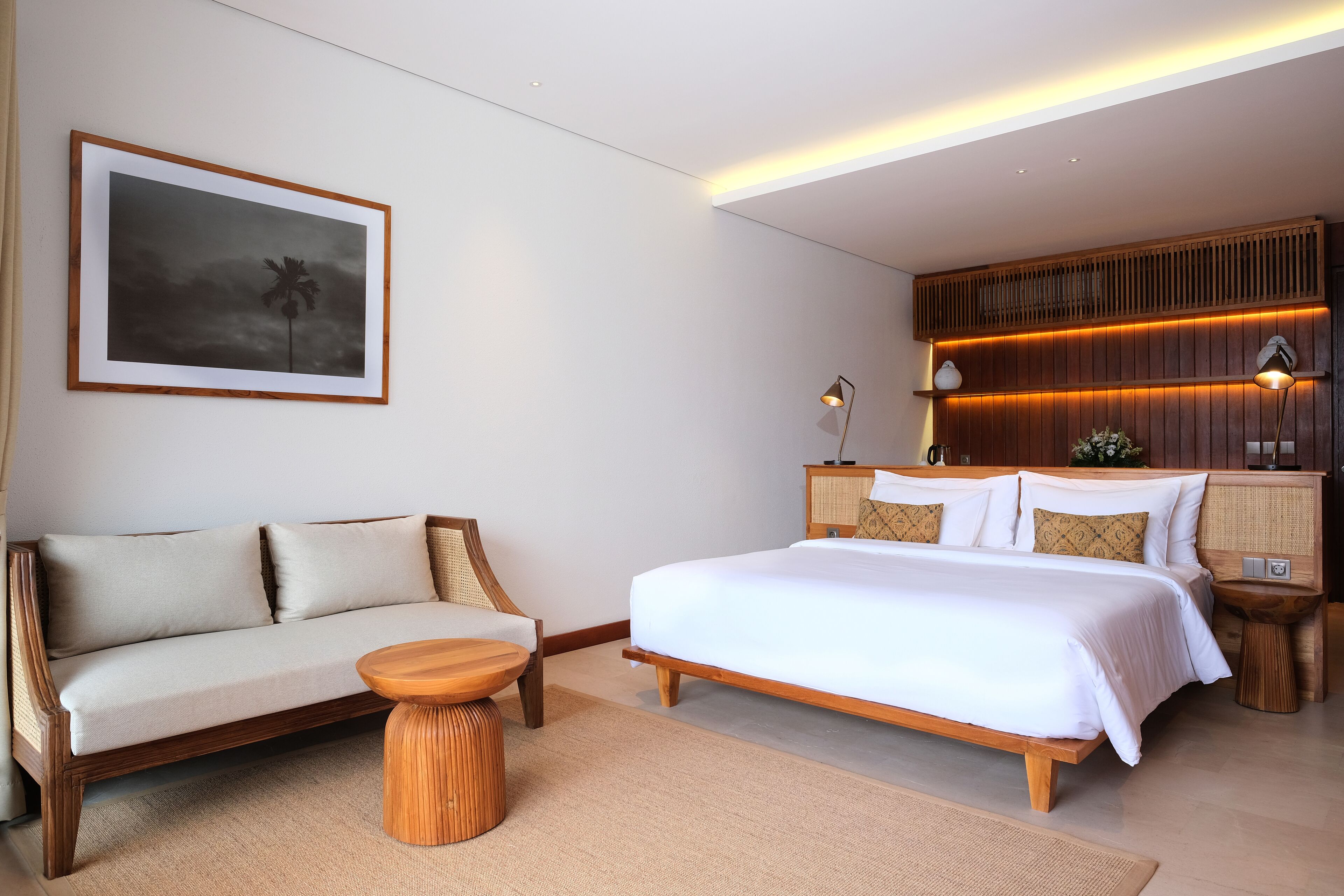 A modern hotel room with a large bed, a sofa, a small round table, and a framed picture on the wall.
