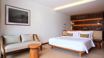 A modern hotel room with a large bed, a sofa, a small round table, and a framed picture on the wall.