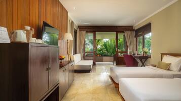 A hotel room with a wooden cabinet, a television, a desk with a chair, two beds, and a view of greenery outside.