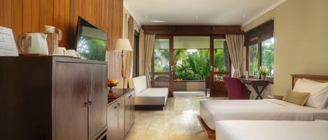 Habitación de hotel con un armario de madera, un televisor, un escritorio con una silla, dos camas y vistas al exterior con vegetación.