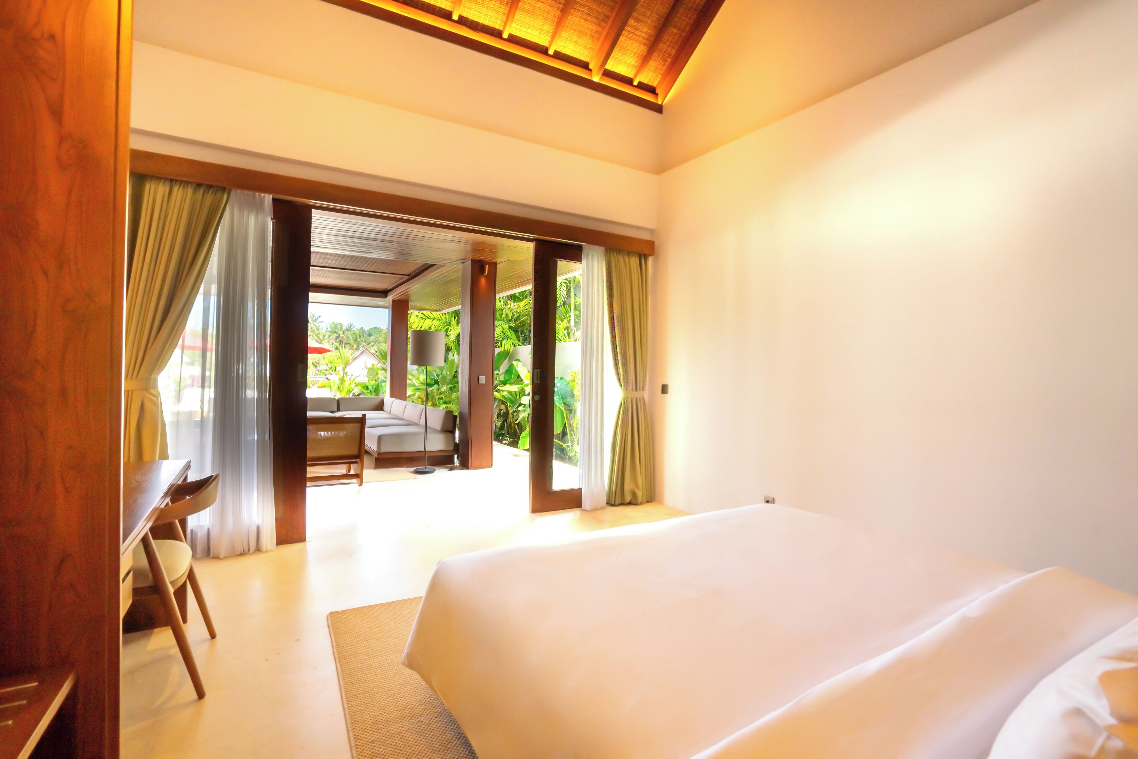 A bedroom with a large bed, wooden furniture, and a view of an outdoor area with a dining table and chairs.